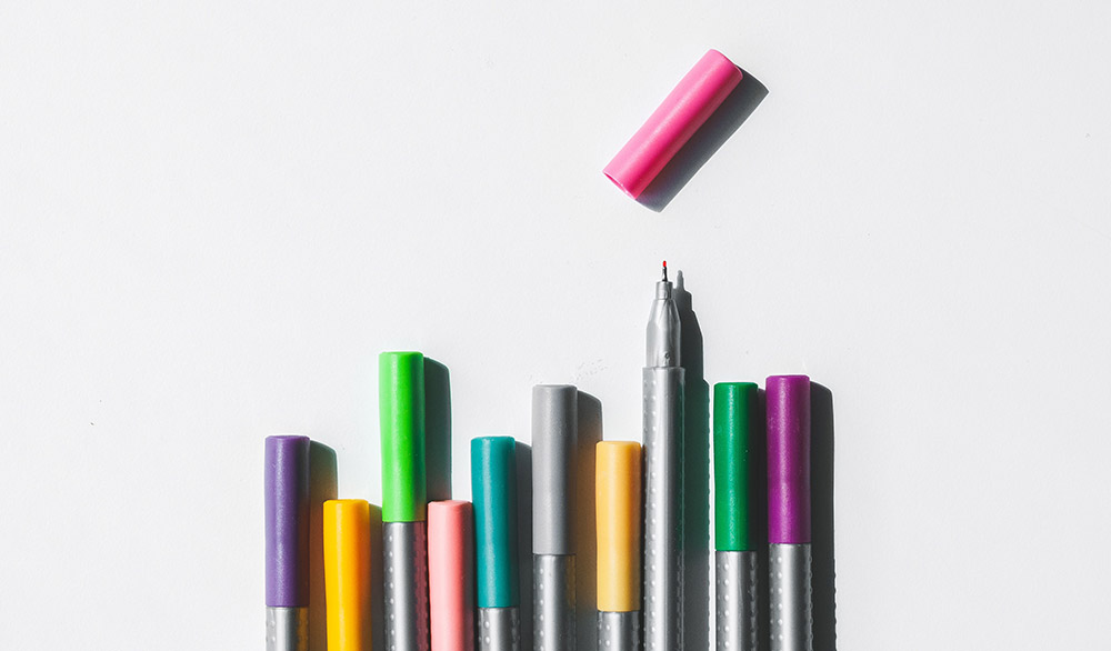 Colorful fine point markers laid out on a grey background