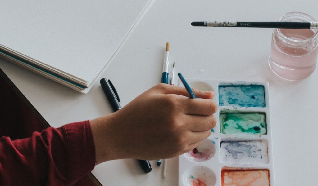 Person getting ready to paint and dipping their brush in watercolor paints