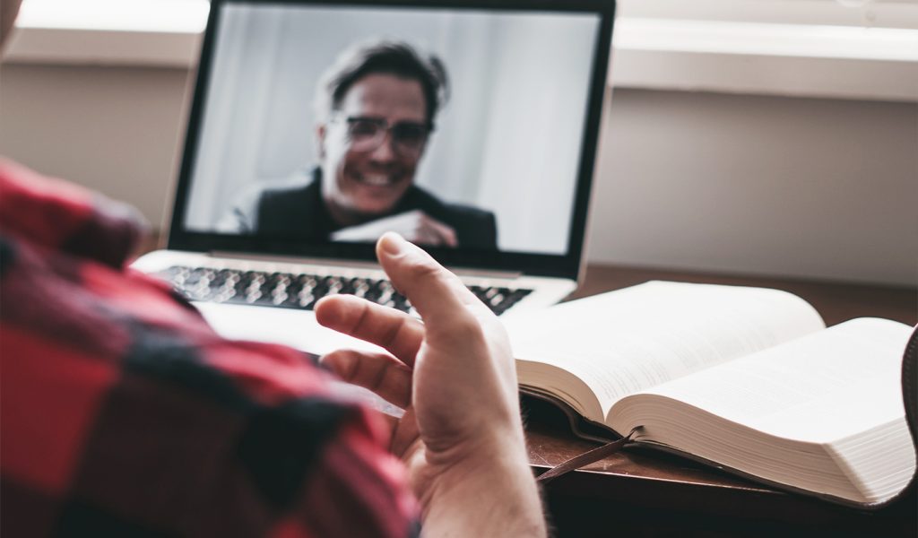 Person speaking with another person on a laptop, with a book open