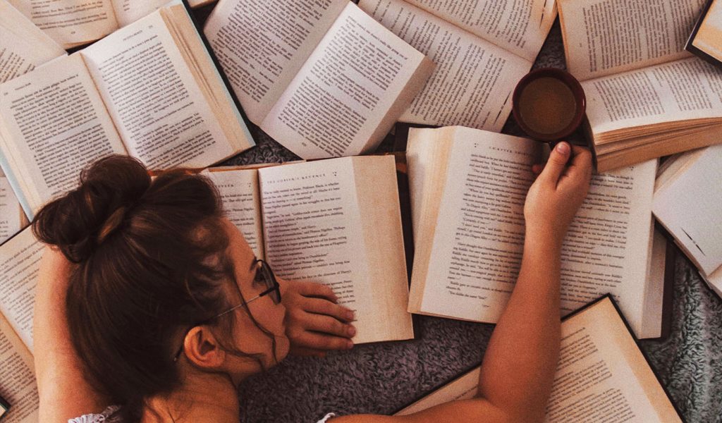 Person resting their head on a lot of open novels.