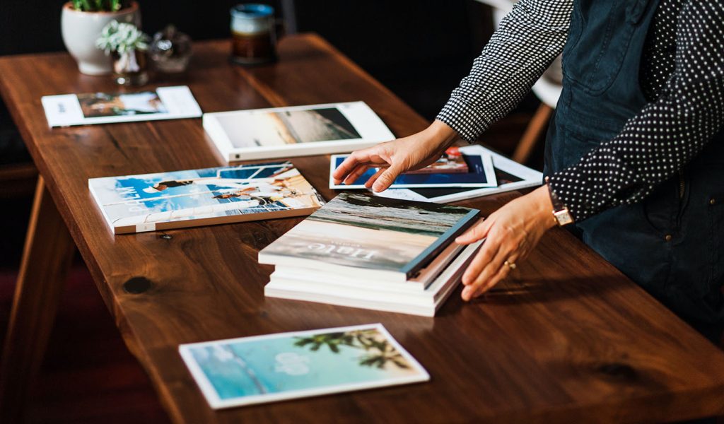 Person sorting through a large stack of magazines on a dark wood table.