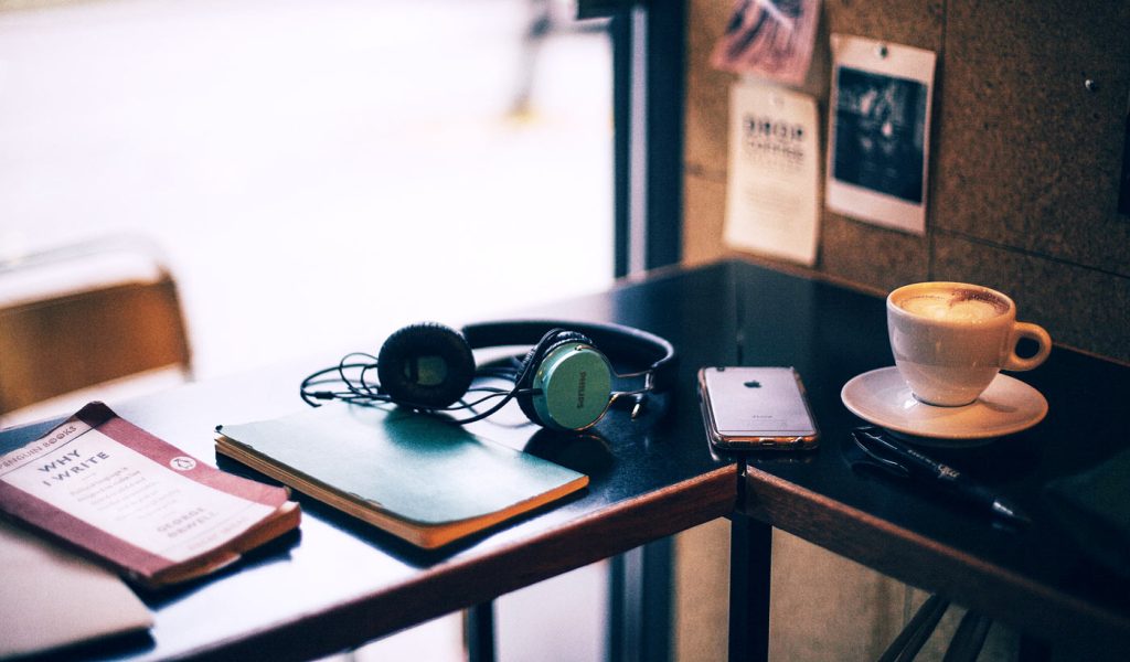 Objects on a table: Why I write book, journal, headphones, iPhone, cappuccino, and pen.